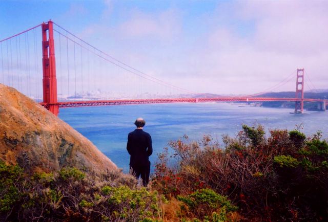 A figure seen from behind on a hillside overlooking the Golden Gate Bridge.