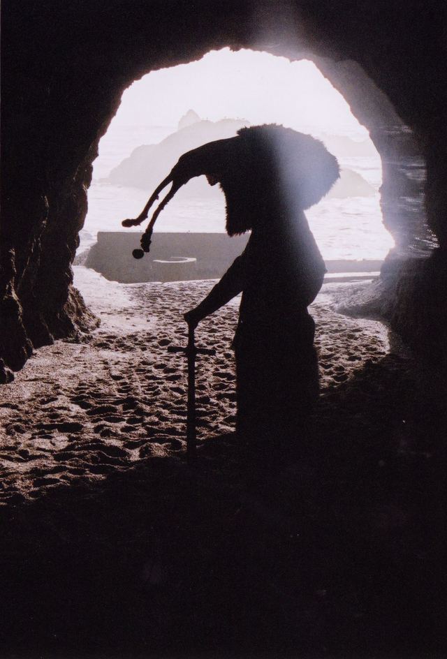 A puppet in silhouette at the mouth of a sea cave.