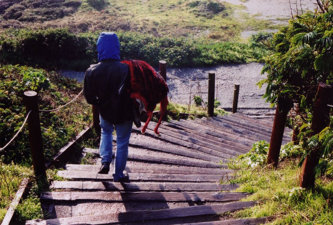 A crew member carries a puppet down a wooden staircase toward the beach.
